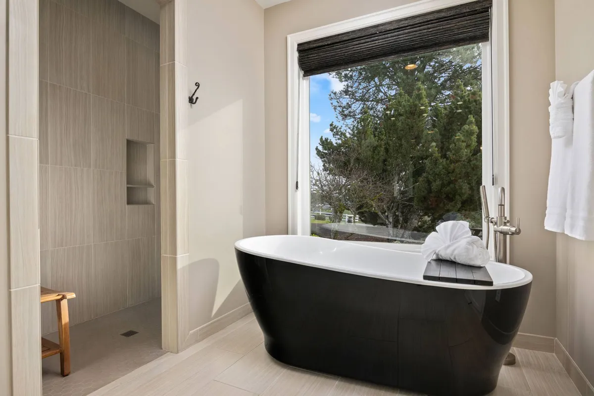A spa-like bathroom with a freestanding soaking tub positioned near a window, a spacious walk-in shower, and a calming, neutral color palette. The layout suggests a focus on relaxation and luxury, enhanced by natural light streaming in.