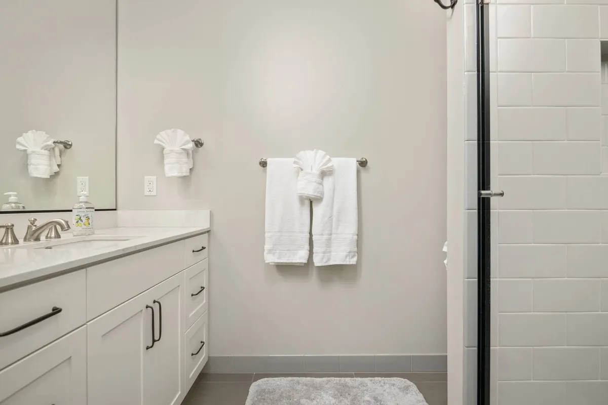 A serene bathroom featuring a vanity with a sink, neatly arranged towels, and a walk-in, doorless shower enclosure. The space is bathed in soft light, evoking a spa-like calm and emphasizing accessibility for all ages and abilities.