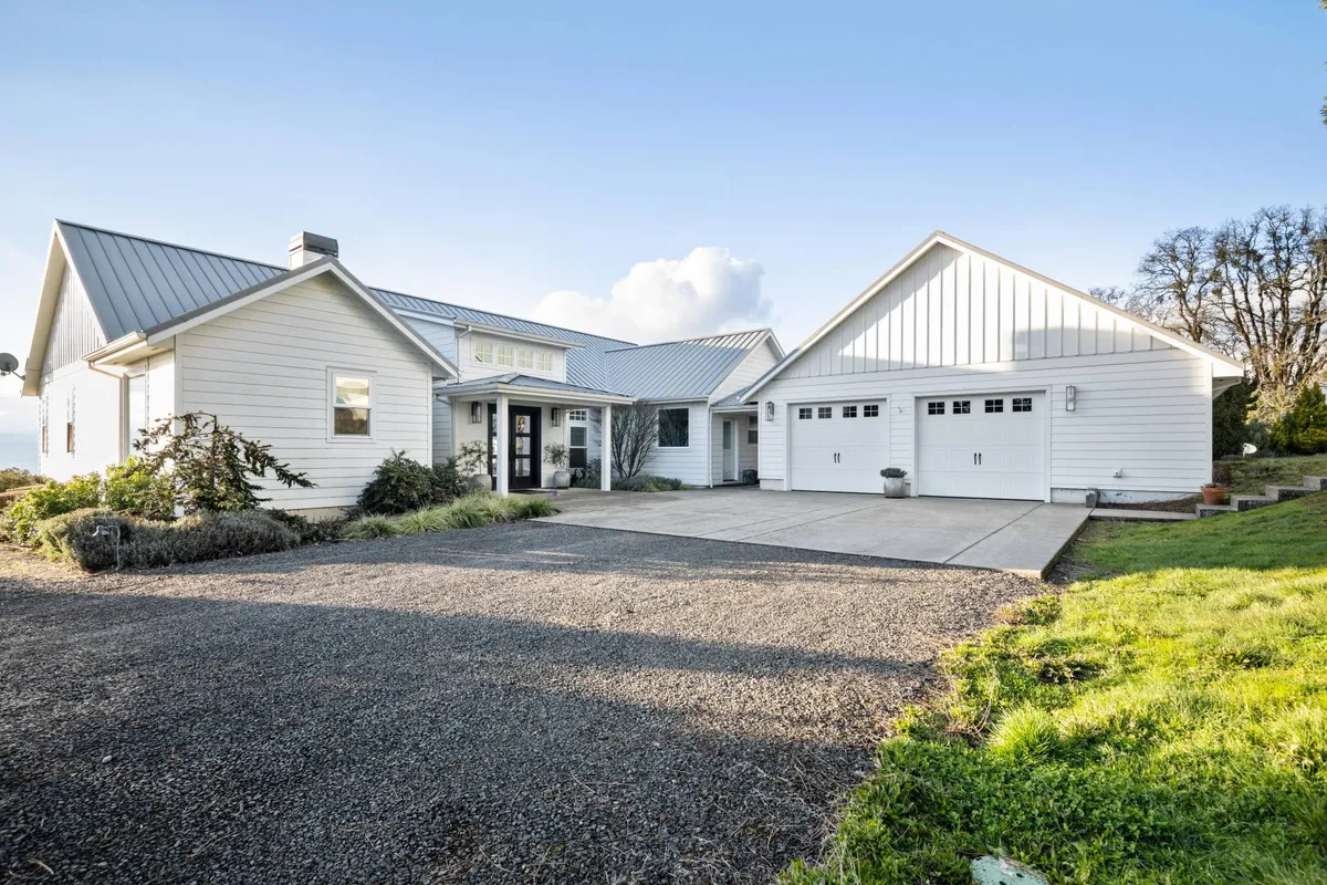 This exterior image captures the main entrance of the home, featuring large windows, a garage door, and a landscaped garden. The welcoming entryway hints at the hospitality and warmth that awaits inside, while the tranquil landscaping reflects the estate’s peaceful setting in the heart of Oregon wine country.