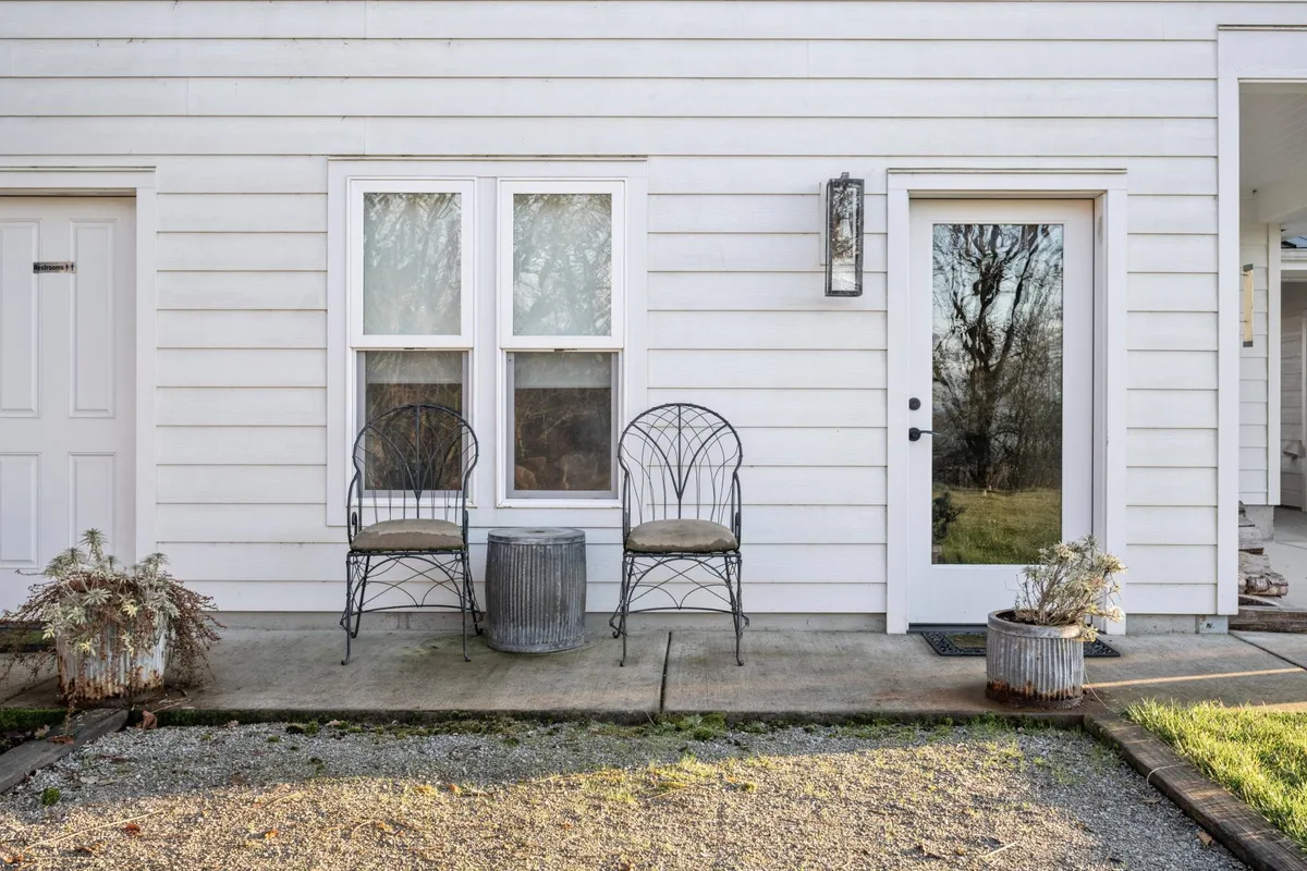 This image features an outdoor patio with two wrought iron chairs, a small metal table, and a potted plant, all set to capture moments of relaxation and connection. The setting is ideal for enjoying the sunset, sipping a drink, or sharing conversations in the open air.