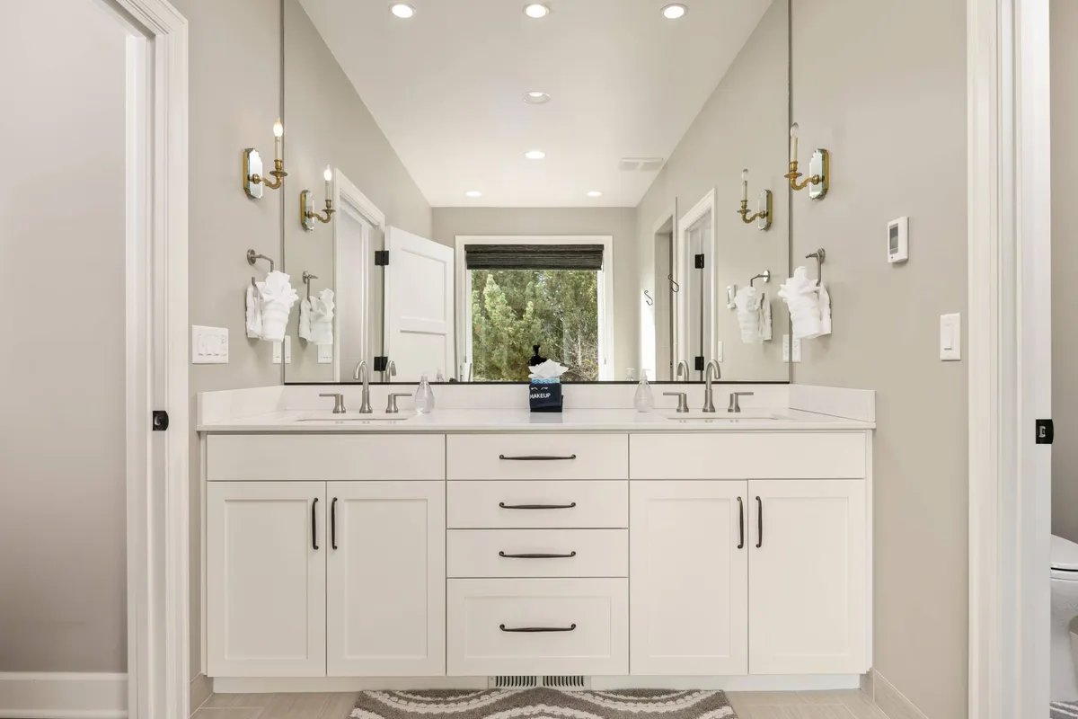 A bright, spa-like bathroom with a double vanity, large mirror, and abundant natural light streaming in from a window. The design exudes relaxation and self-care, reminiscent of a boutique day spa experience.
